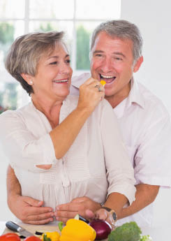 Woman feeding pepper to man in kitchen