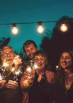 Happy family celebrating with sparkler at night party outdoor - Group of people with different ages and ethnicity having fun together outside - Friendship, eve and celebration concept