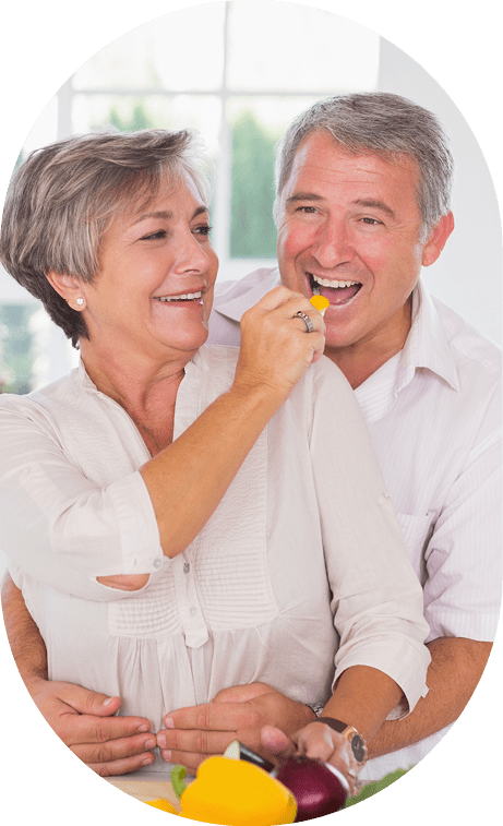 Woman feeding pepper to man in kitchen